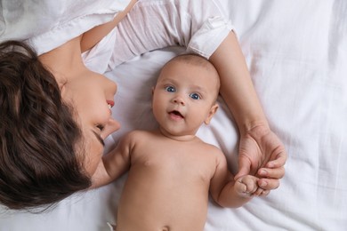 Photo of Happy young mother with her cute baby on bed, top view