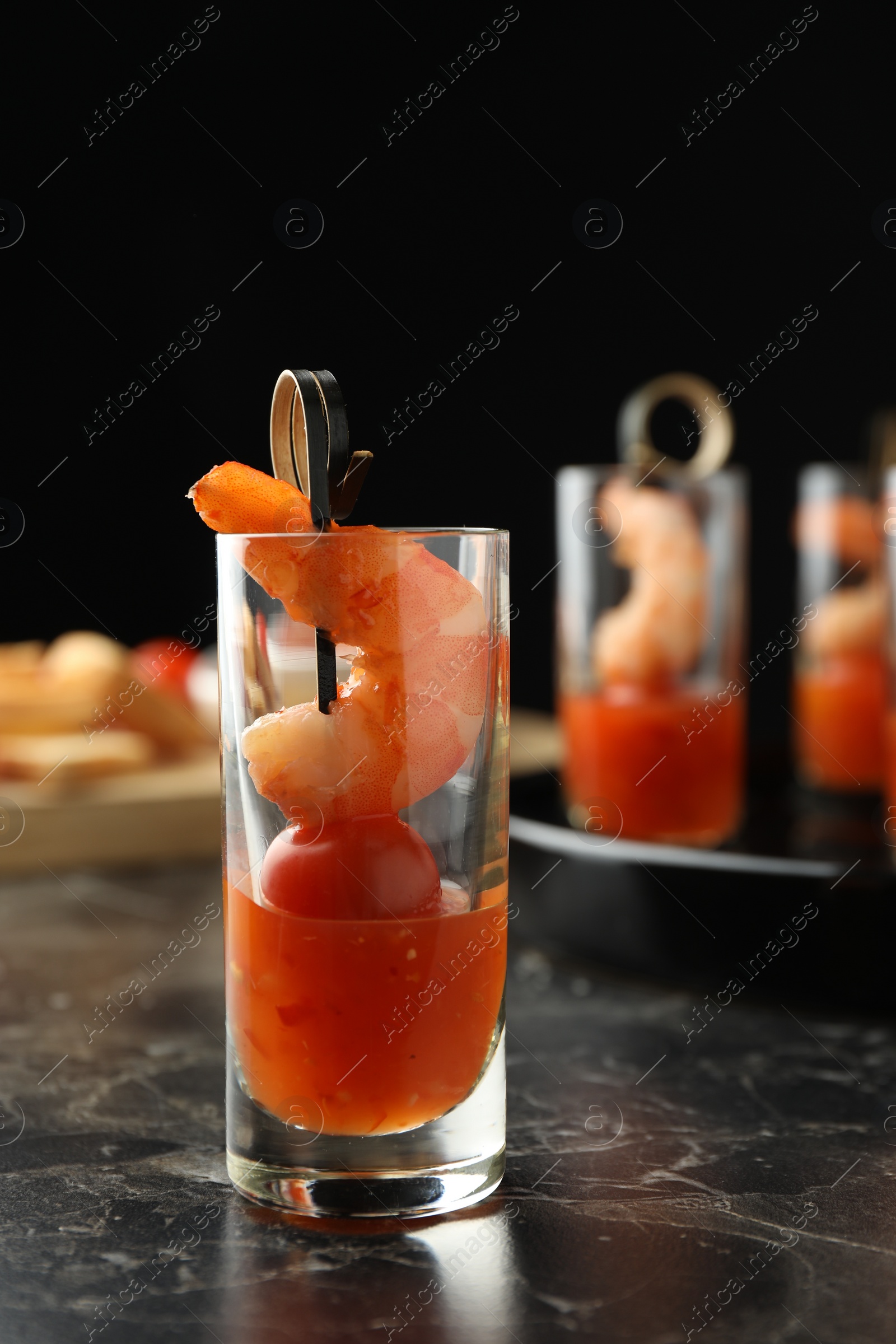 Photo of Tasty canape with shrimp, tomato and sauce in shot glass on black marble table, closeup