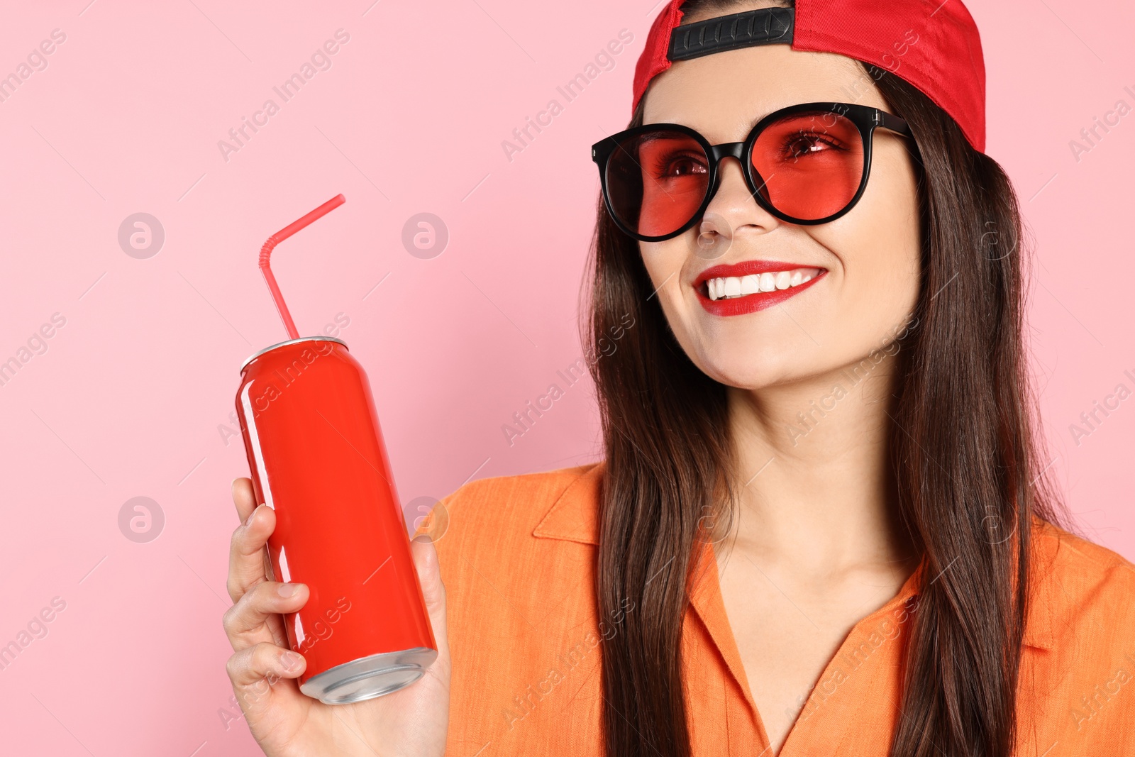 Photo of Beautiful young woman in stylish sunglasses holding tin can with beverage on pink background, closeup