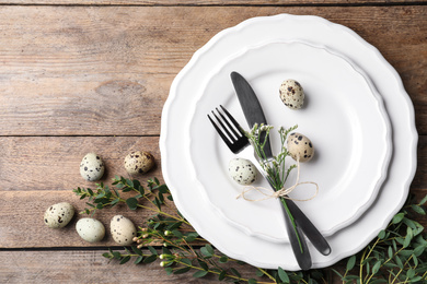 Festive Easter table setting with quail eggs and floral decor on wooden background, top view