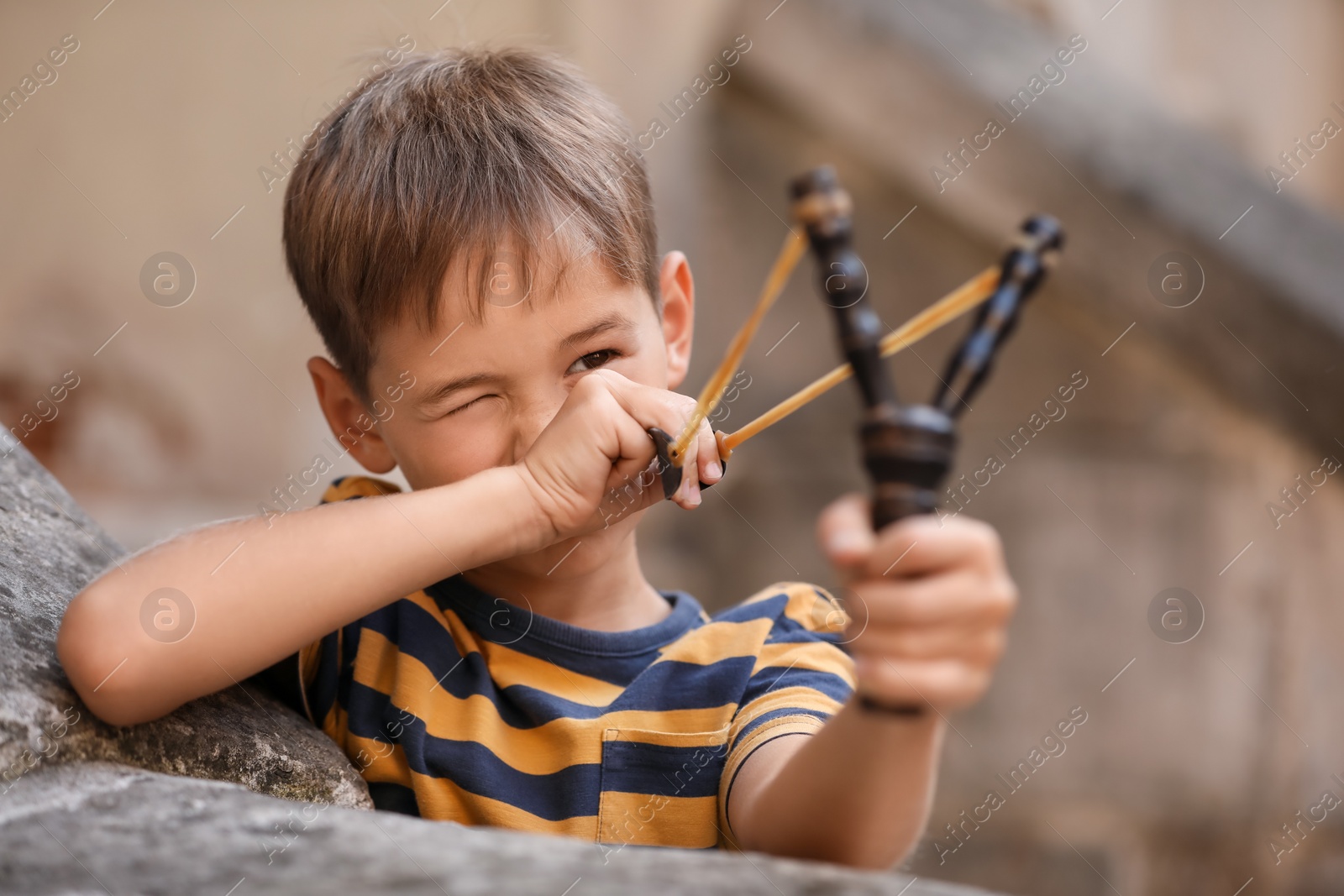 Photo of Cute little boy playing with slingshot outdoors