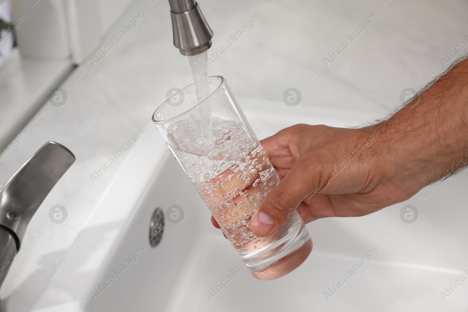 Photo of Man filling glass with water from tap at home, closeup