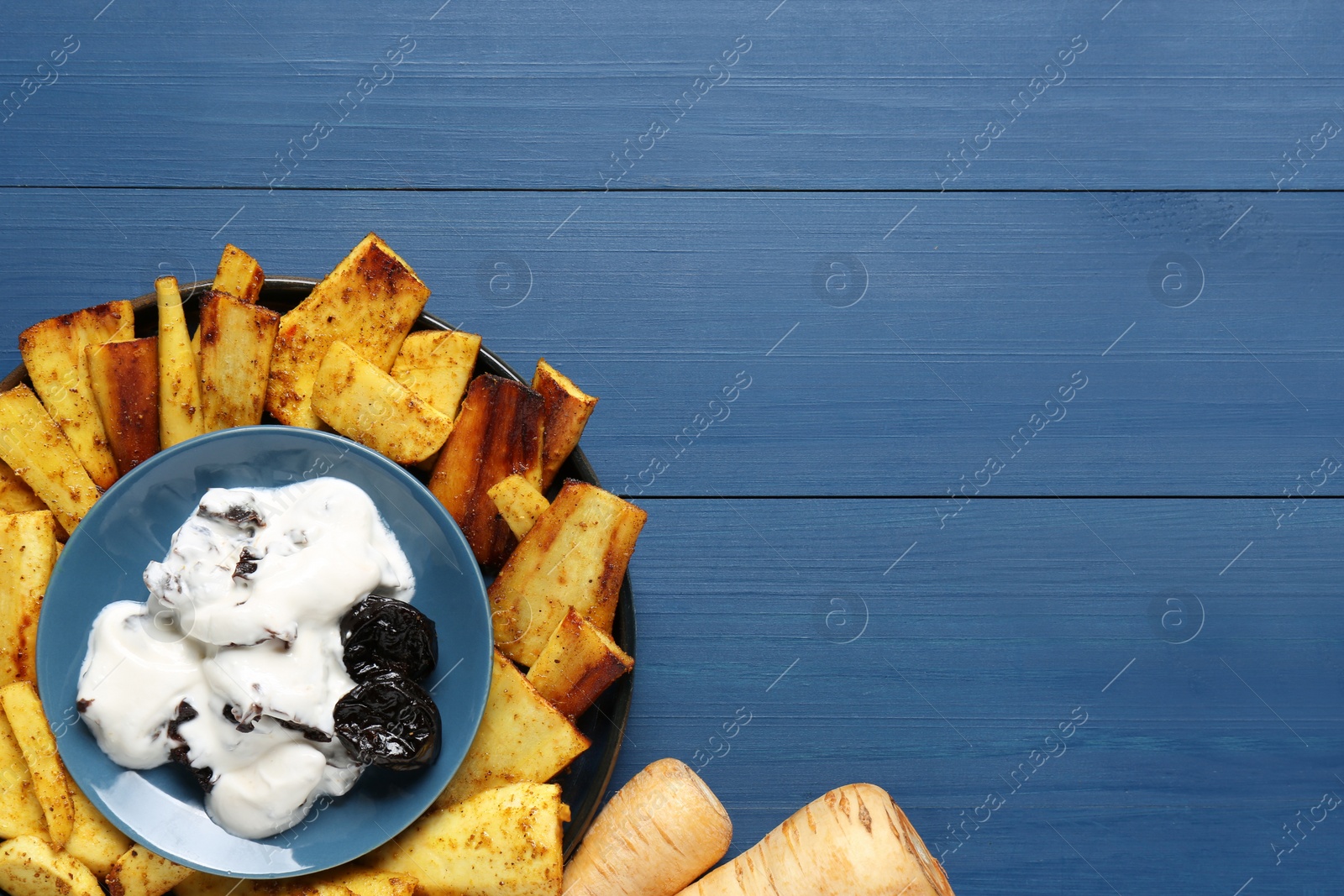 Photo of Delicious parsnips and prunes in cream sauce on blue wooden table, flat lay. Space for text