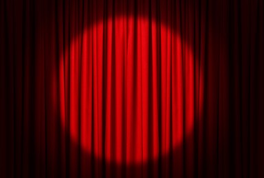 Image of Spotlight illuminating closed red stage curtains. Start of performance 