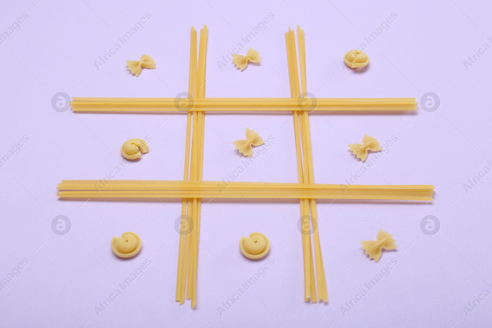 Photo of Tic tac toe game made with different types of pasta on lilac background