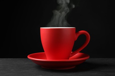 Red cup with hot steaming coffee on grey table against black background