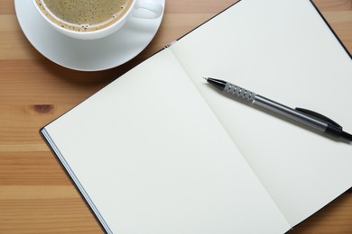 Photo of Empty notebook, pen and cup of coffee on wooden table, flat lay