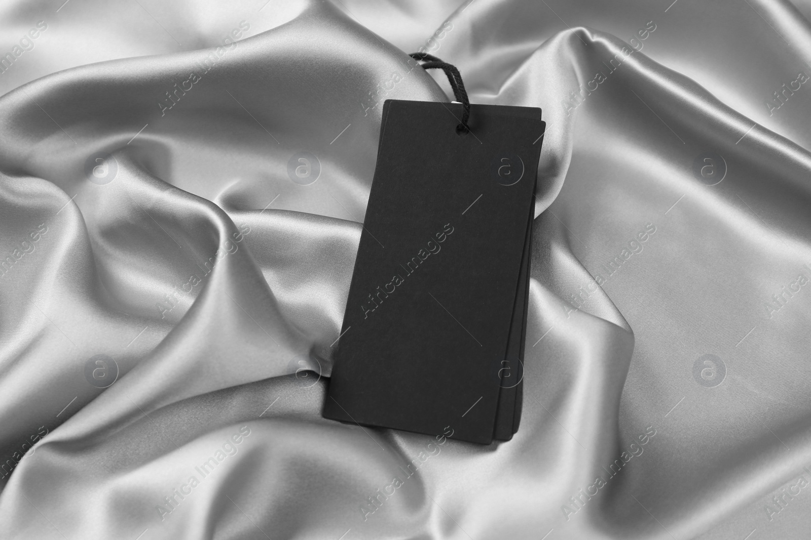 Photo of Blank black tags on silver silky fabric. Space for text