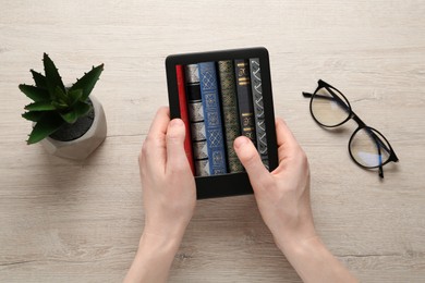 Woman using e-book reader at wooden table, top view