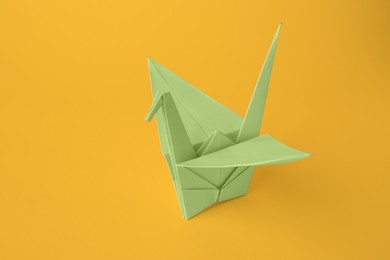 Photo of Origami art. Beautiful light green paper crane on orange background