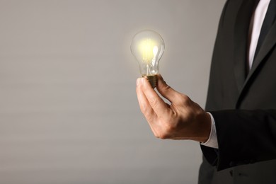 Glow up your ideas. Closeup view of businessman holding light bulb on grey background, space for text