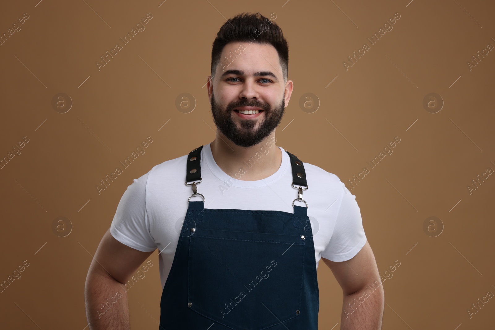 Photo of Smiling man in kitchen apron on brown background. Mockup for design