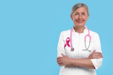 Photo of Doctor with pink ribbon and stethoscope on light blue background, space for text. Breast cancer awareness