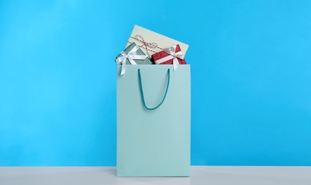 Photo of Paper shopping bag full of gift boxes on light blue background