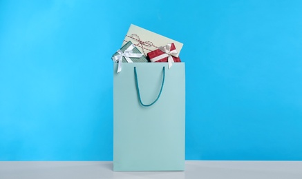 Paper shopping bag full of gift boxes on light blue background