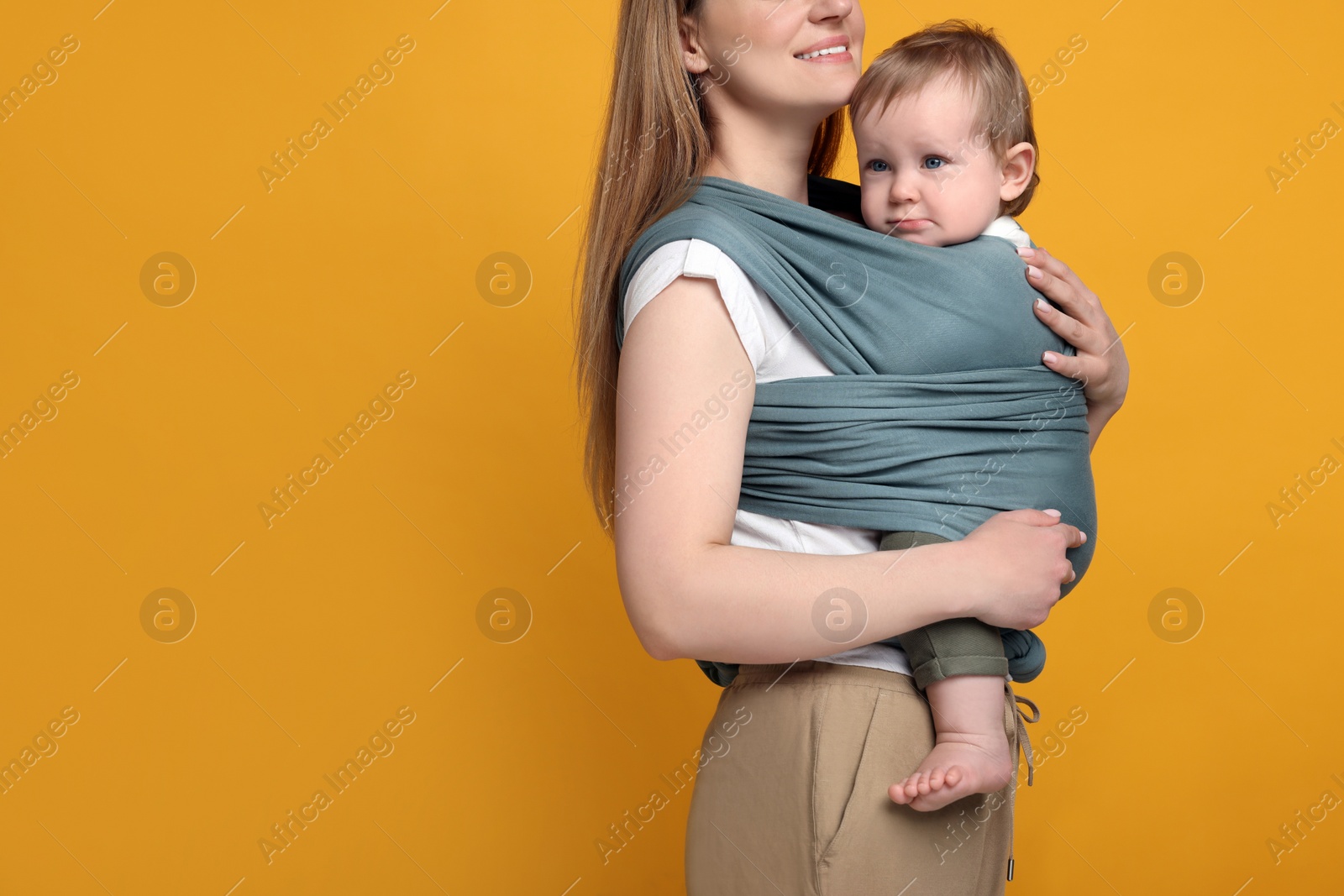 Photo of Mother holding her child in baby wrap on orange background, closeup. Space for text