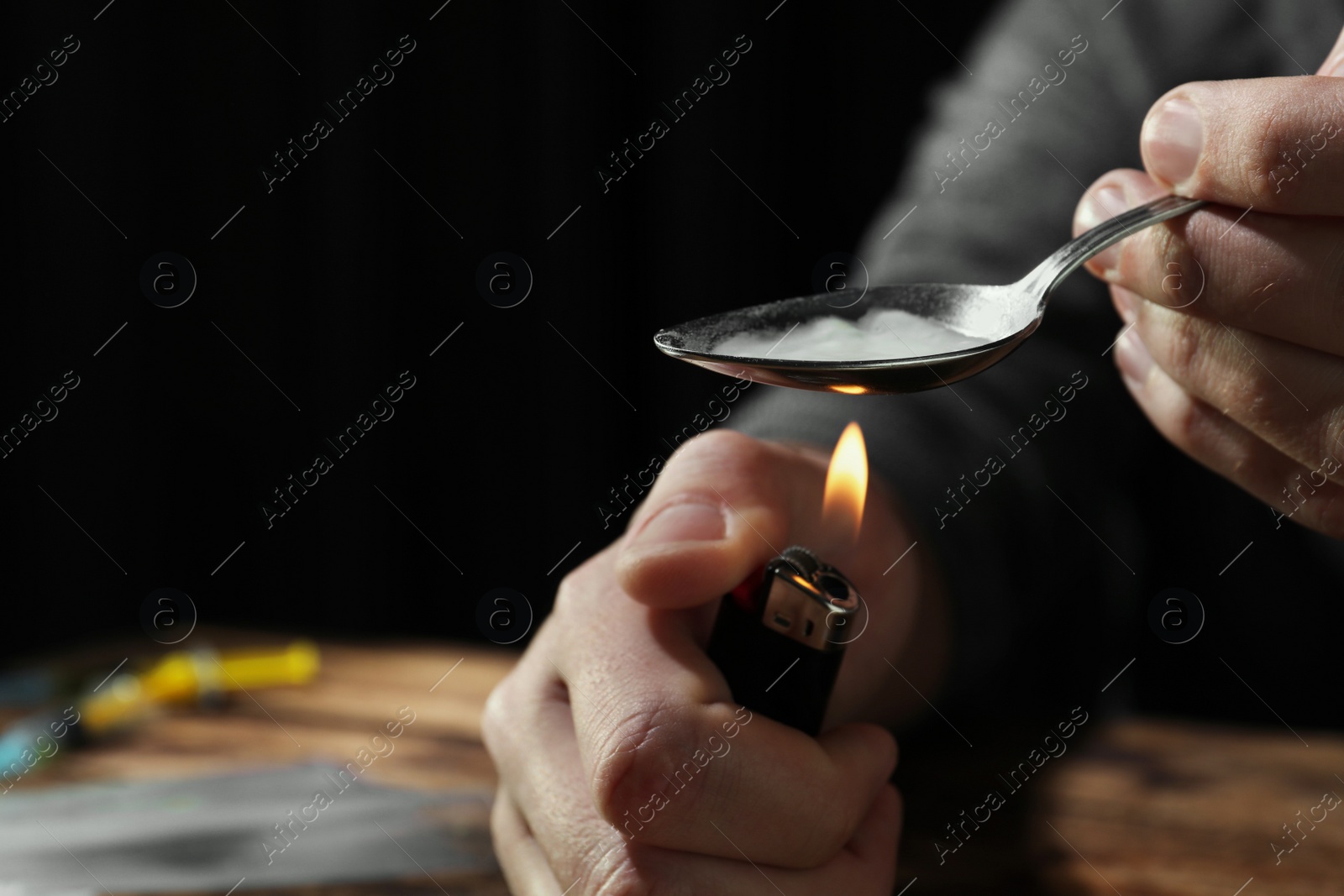 Photo of Man preparing drugs with spoon and lighter at wooden table, closeup. Space for text