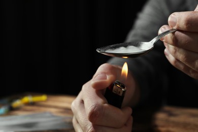 Photo of Man preparing drugs with spoon and lighter at wooden table, closeup. Space for text