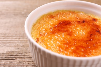 Delicious creme brulee in bowl on wooden table, closeup