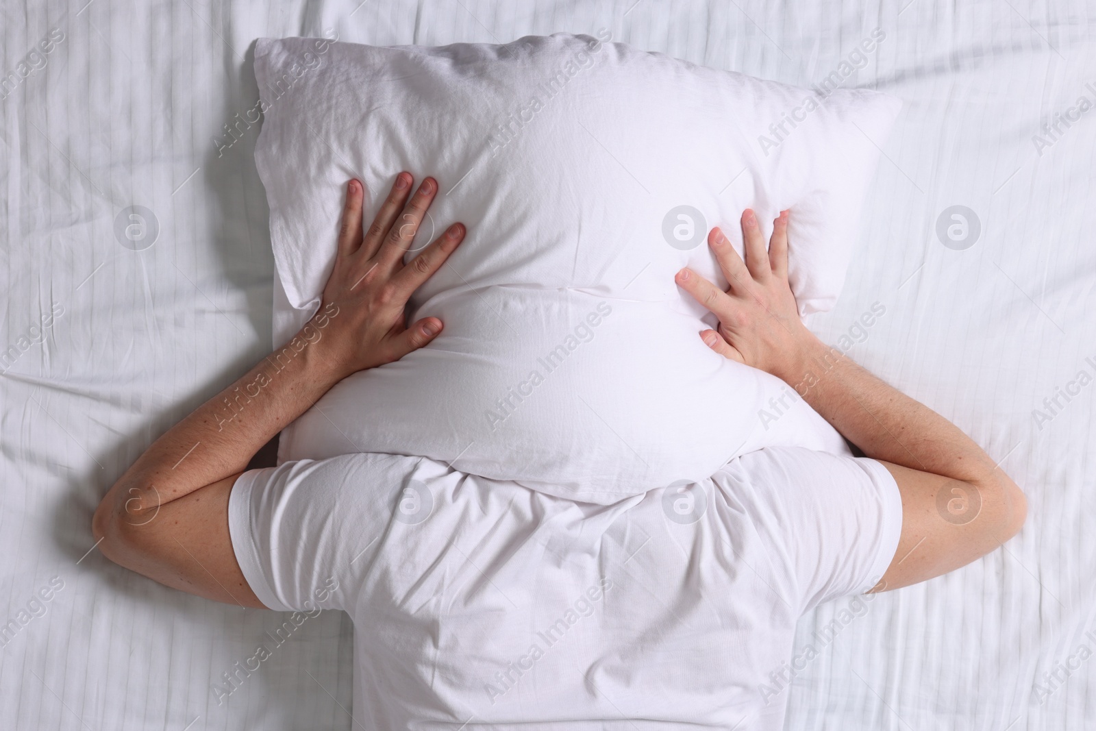 Photo of Man covering his head with pillow in bed, top view. Insomnia problem