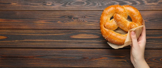 Image of Woman with tasty freshly baked pretzel at wooden table, top view with space for text. Banner design
