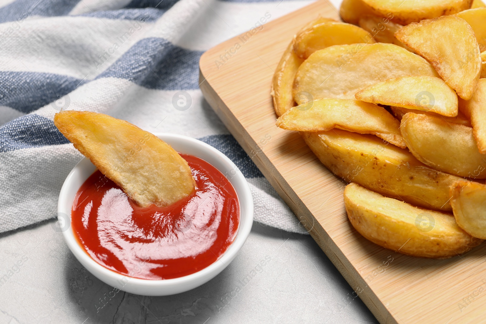 Photo of Delicious baked potato wedges and ketchup in bowl on light gray table, closeup