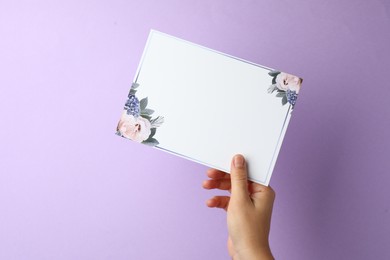 Woman holding blank invitation card on lilac background, closeup. Space for text