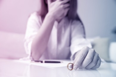 Woman with wedding ring at table indoors, closeup. Cheating and breakup