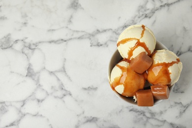 Photo of Delicious ice cream with caramel and sauce in bowl on marble table. Space for text