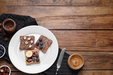Photo of Different tasty toasts with nut butter and products on wooden table, flat lay. Space for text