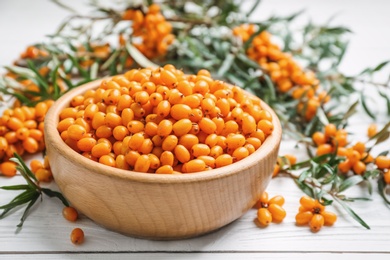 Fresh ripe sea buckthorn in bowl on white wooden table, closeup