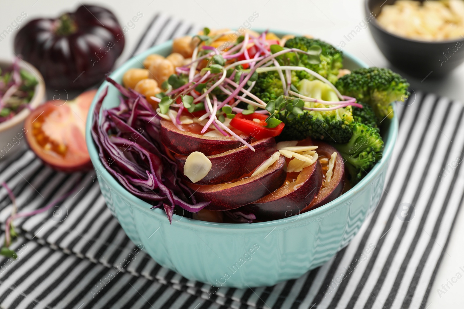 Photo of Delicious vegan bowl with broccoli, red cabbage and black tomato on table, closeup