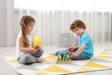 Cute little children playing with set of wooden geometric figures on floor in kindergarten