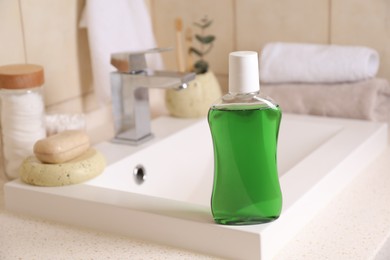 Fresh mouthwash in bottle on sink in bathroom, closeup. Space for text