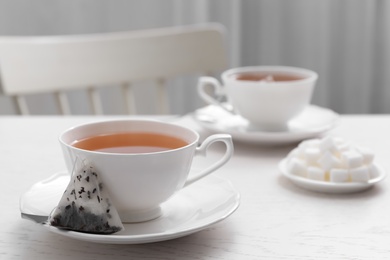 Tea bag and cup of hot drink on white wooden table. Space for text