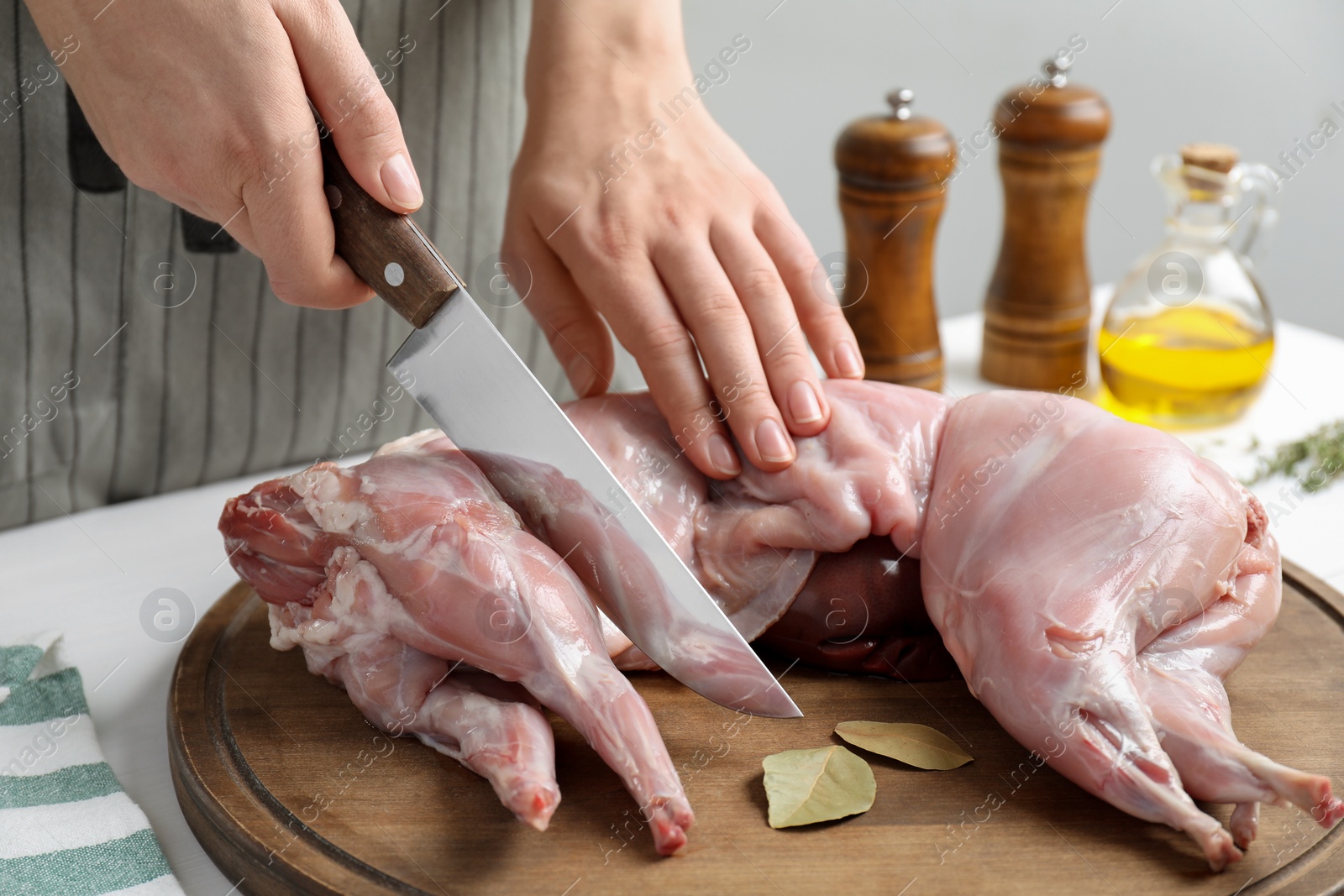 Photo of Woman cutting whole raw rabbit at white wooden table, closeup
