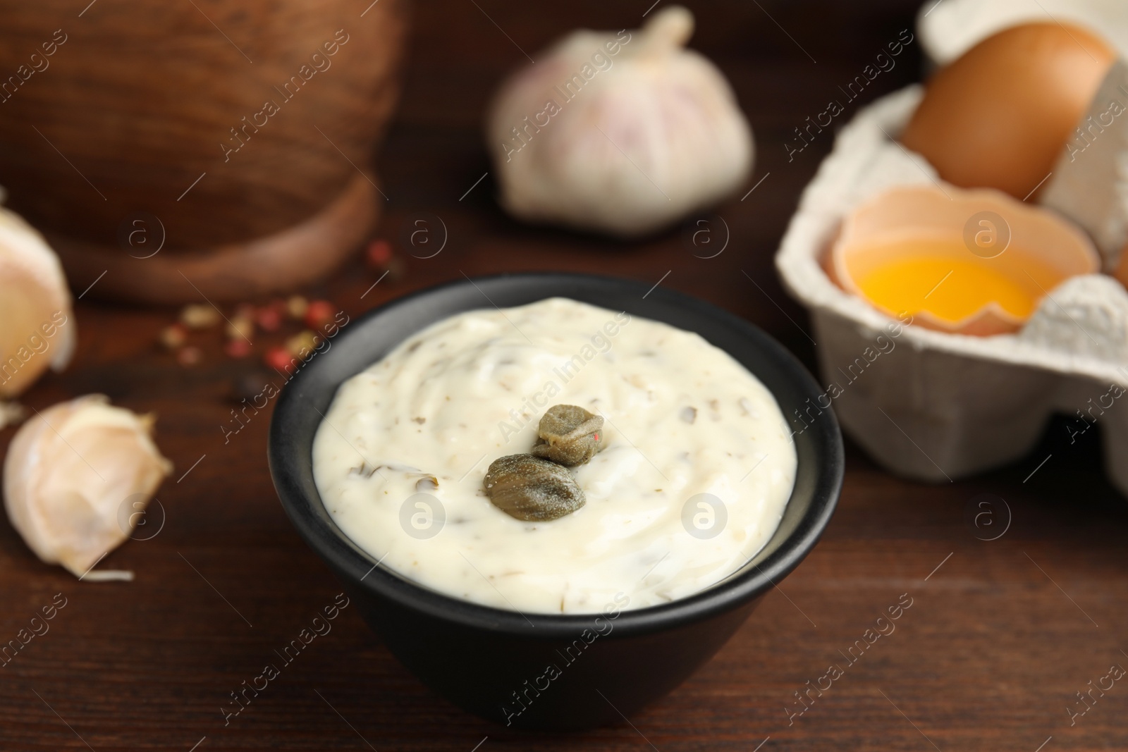 Photo of Creamy caper sauce in bowl on wooden table, closeup