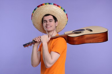 Young man in Mexican sombrero hat with guitar on violet background