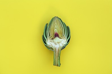 Photo of Cut fresh raw artichoke on yellow background, top view