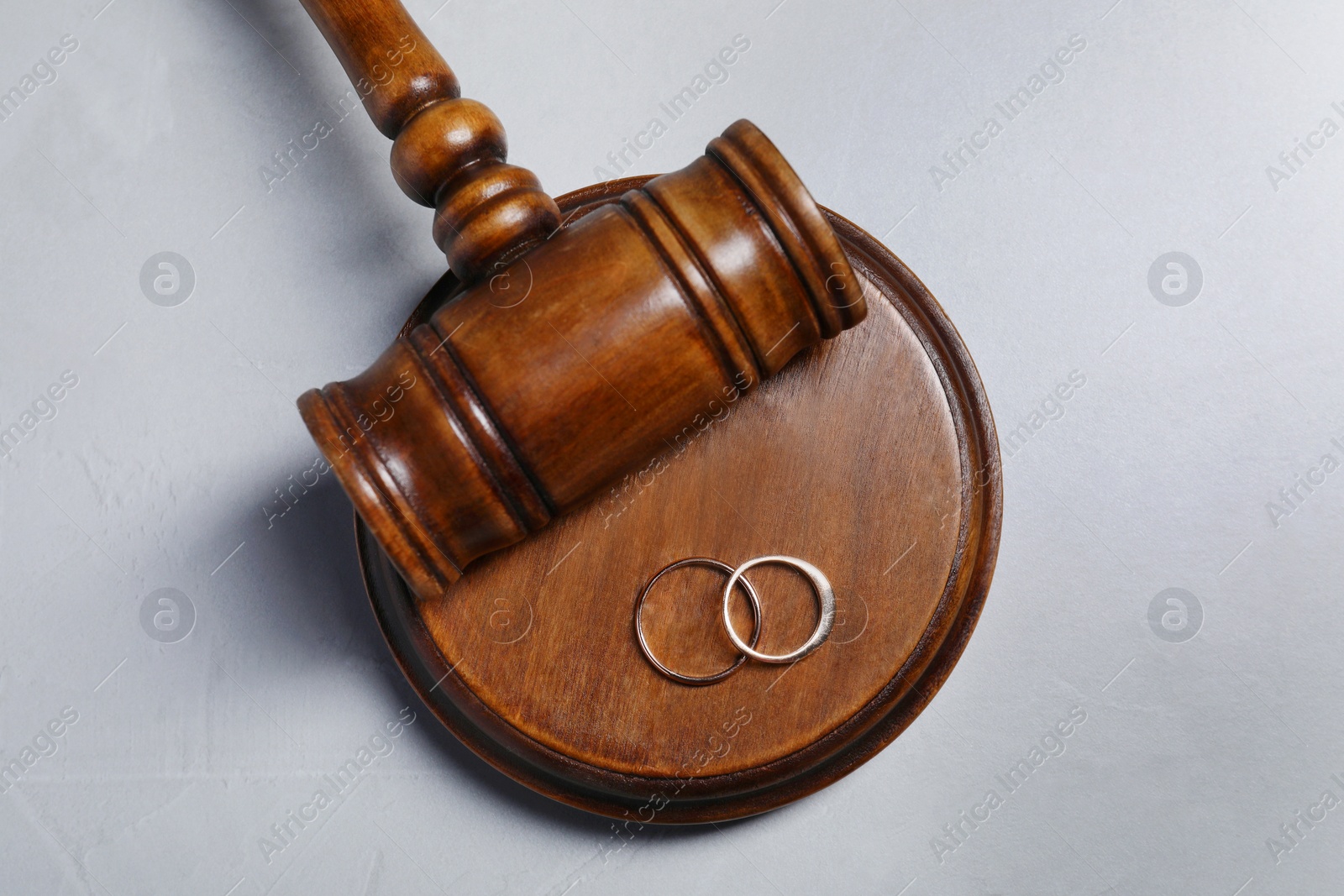 Photo of Divorce process. Wooden gavel and wedding rings on grey textured table, flat lay