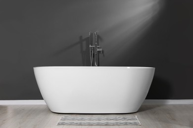 Stylish ceramic tub near grey wall in bathroom
