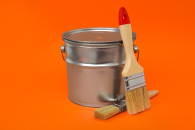 Photo of Can of orange paint and brushes on color background