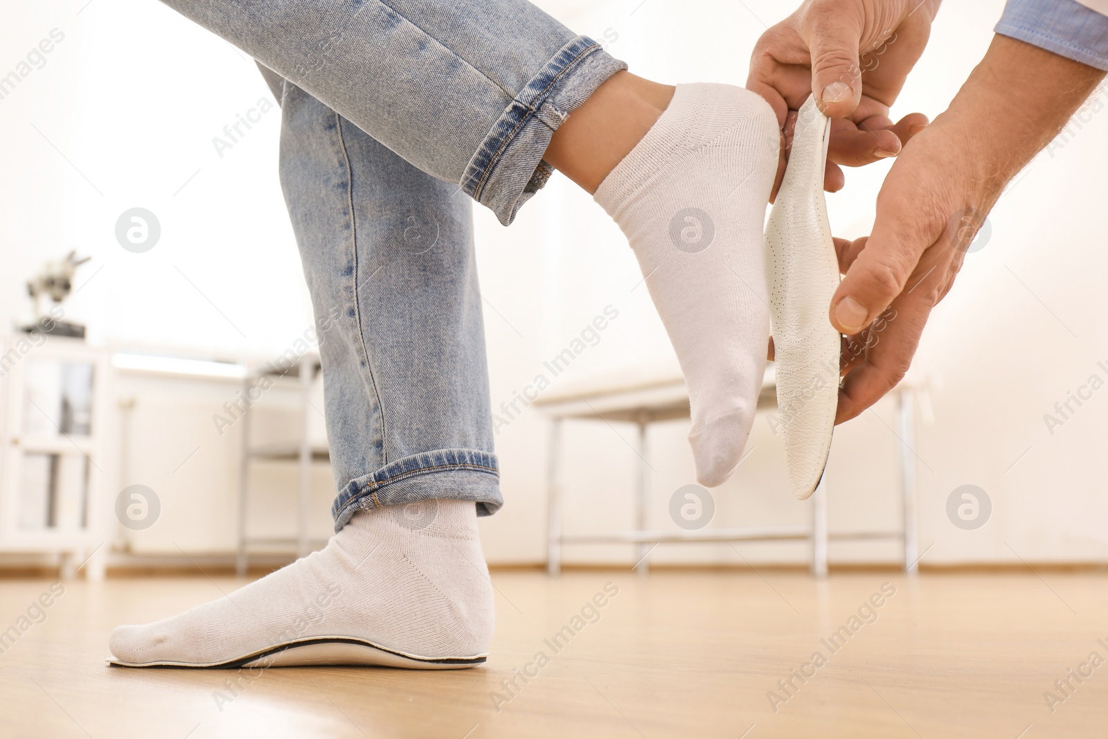 Photo of Male orthopedist fitting insole on patient's foot in clinic, closeup