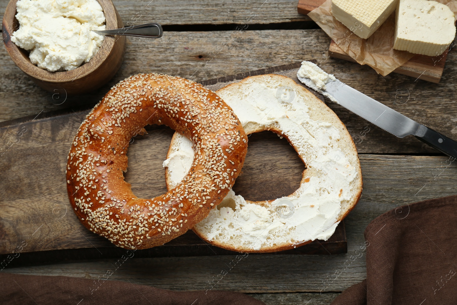 Photo of Delicious bagel with tofu cream cheese and knife on wooden table, flat lay