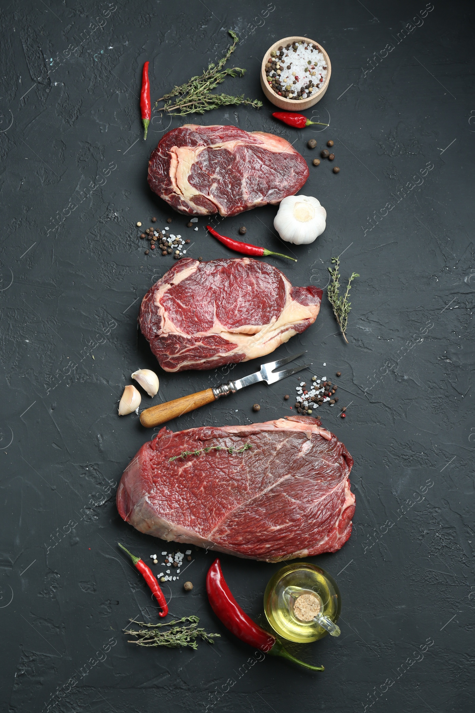 Photo of Pieces of raw beef meat, products and spices on black textured table, flat lay