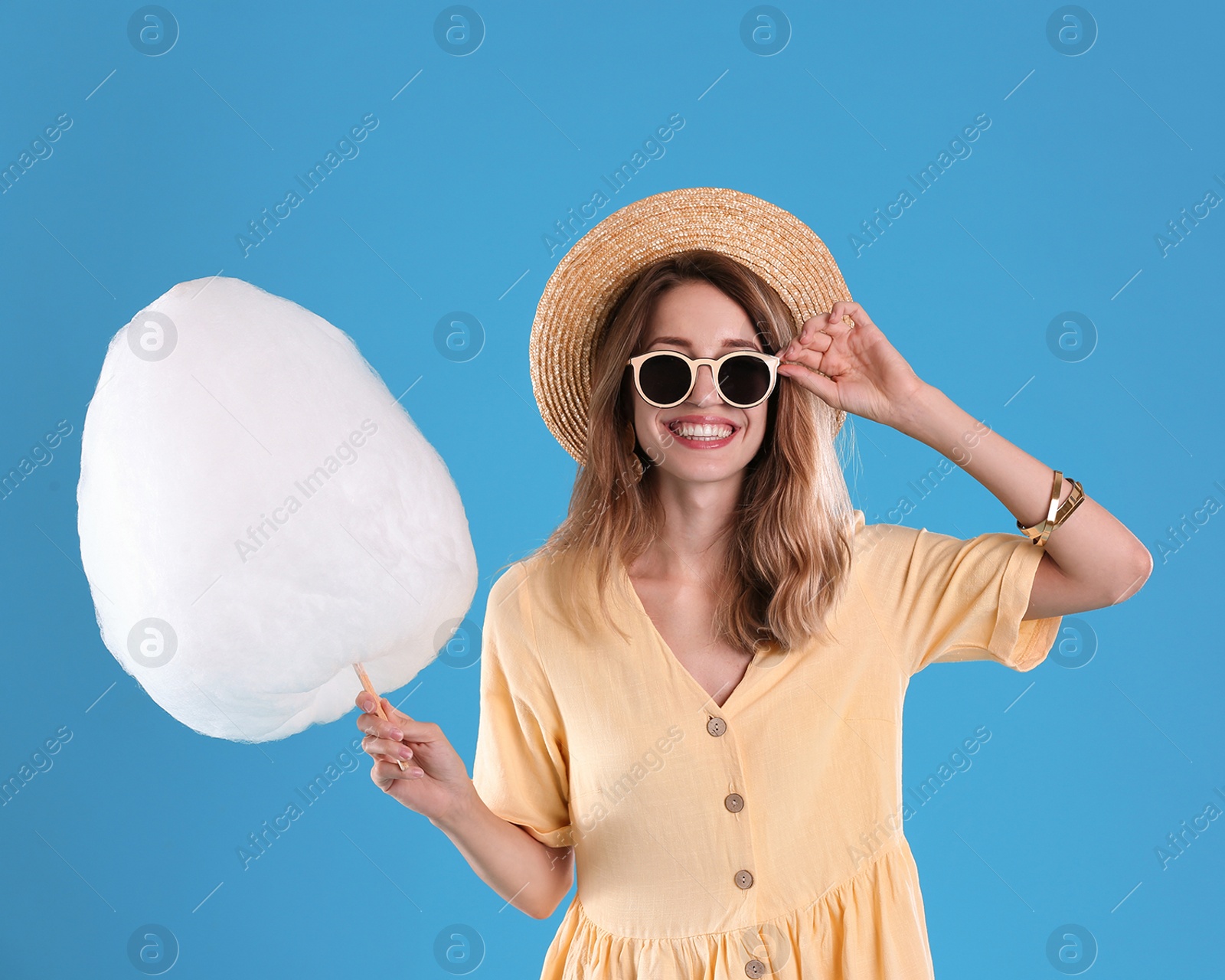 Photo of Happy young woman with cotton candy on blue background