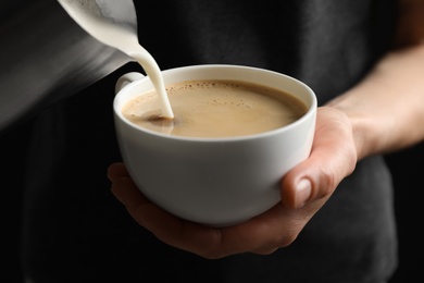 Photo of Woman pouring milk into cup of hot coffee, closeup