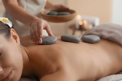 Photo of Beautiful young woman getting hot stone massage in spa salon