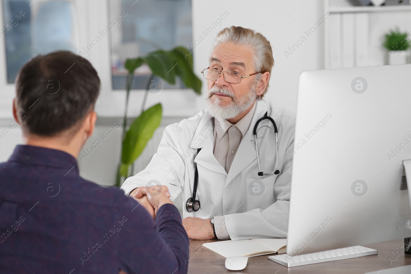 Photo of Senior doctor shaking hands with patient at wooden table in clinic