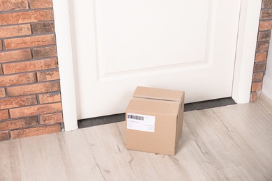 Photo of Cardboard parcel box on floor near apartment entrance. Mockup for design